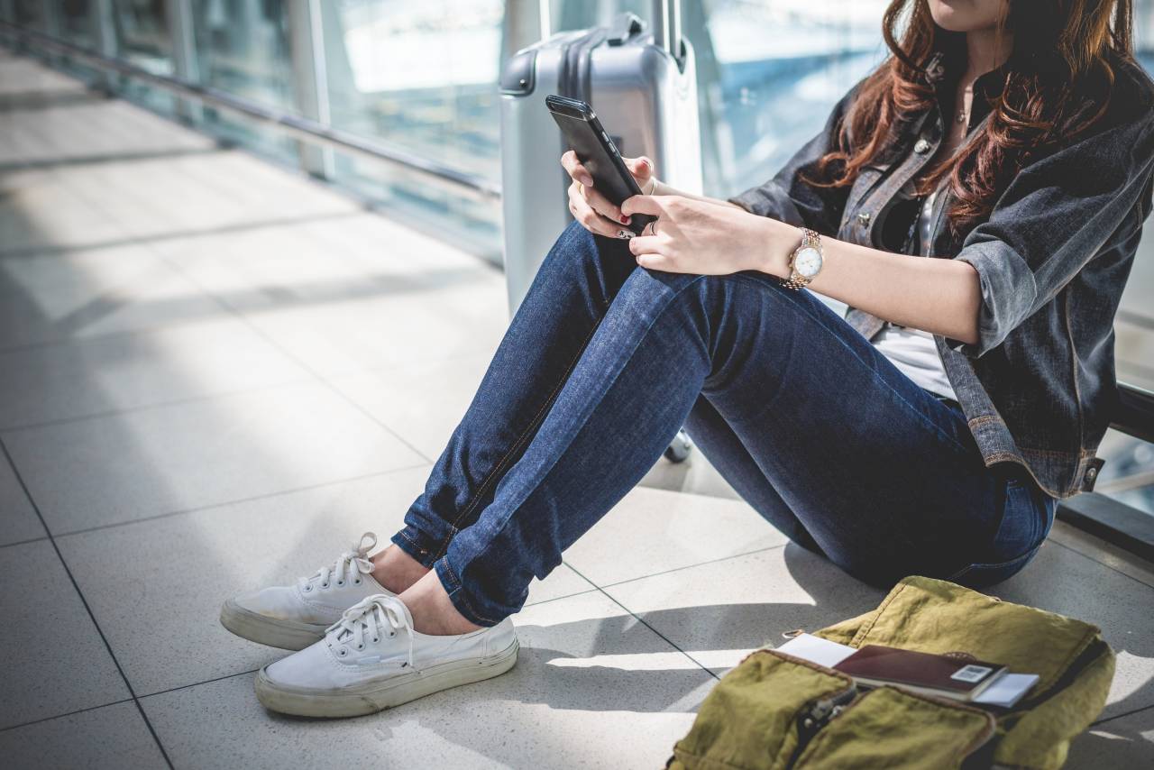 Ztráta dokladů v zahraničí - Žena s mobilem sedící na letišti